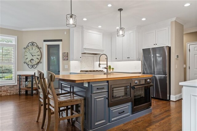 kitchen with butcher block counters, freestanding refrigerator, white cabinetry, an island with sink, and oven