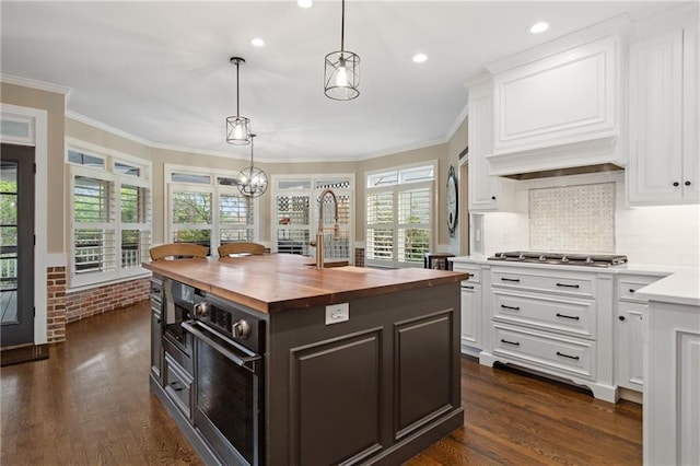 kitchen with a center island with sink, stainless steel gas cooktop, wood counters, ornamental molding, and white cabinetry