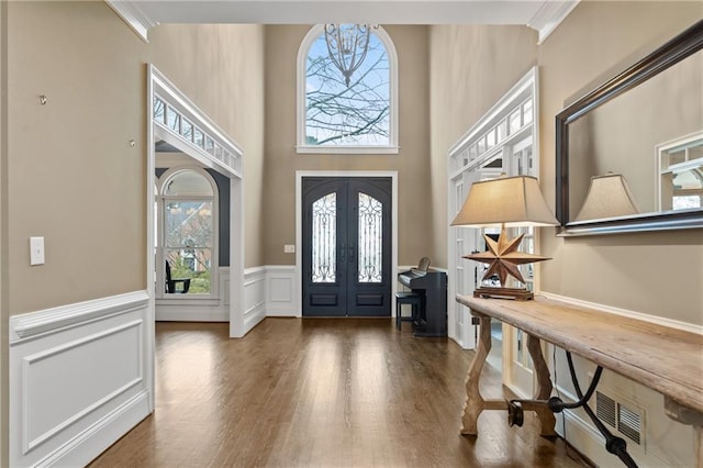 foyer entrance with french doors, a wainscoted wall, visible vents, and dark wood-style flooring