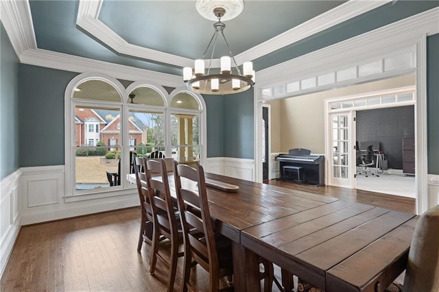 dining space with a raised ceiling, a wainscoted wall, dark wood-style flooring, french doors, and a chandelier