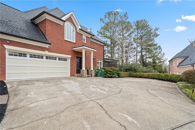 traditional home featuring a garage, roof with shingles, concrete driveway, and brick siding