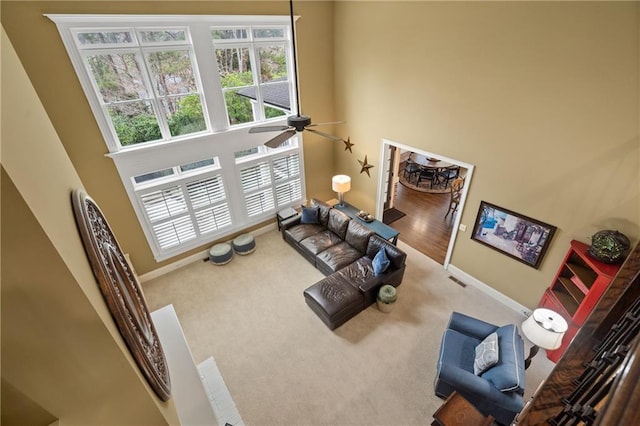 living area with a high ceiling, carpet flooring, a ceiling fan, and baseboards