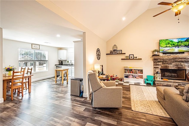 living area featuring lofted ceiling, ceiling fan, a stone fireplace, dark wood-type flooring, and baseboards