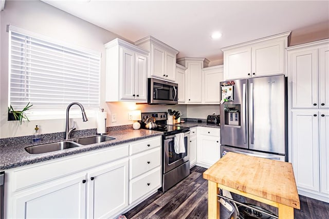 kitchen featuring dark countertops, white cabinets, stainless steel appliances, and a sink