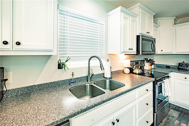 kitchen with stainless steel appliances, dark wood-style flooring, a sink, white cabinetry, and dark stone countertops