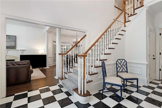 staircase featuring ornate columns, crown molding, hardwood / wood-style floors, and an inviting chandelier