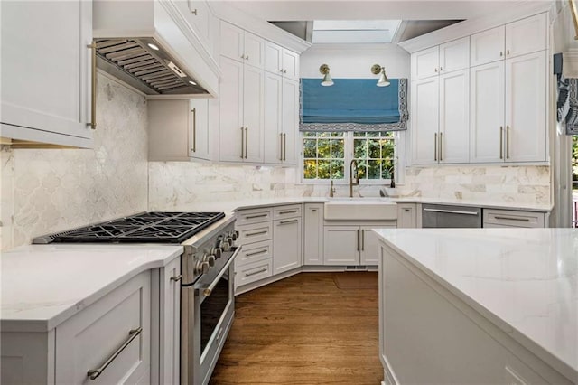 kitchen featuring sink, custom exhaust hood, white cabinetry, appliances with stainless steel finishes, and light hardwood / wood-style floors