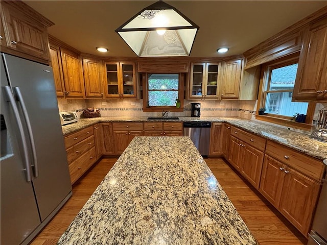 kitchen with light stone counters, sink, backsplash, appliances with stainless steel finishes, and light hardwood / wood-style floors