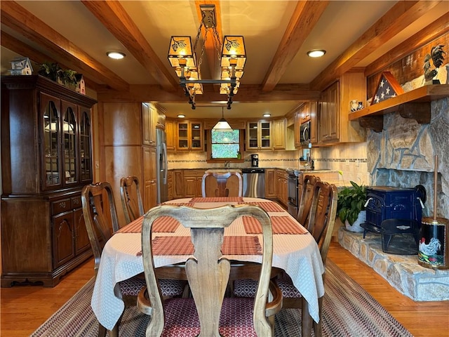 dining room featuring wood-type flooring, beamed ceiling, sink, and a wood stove