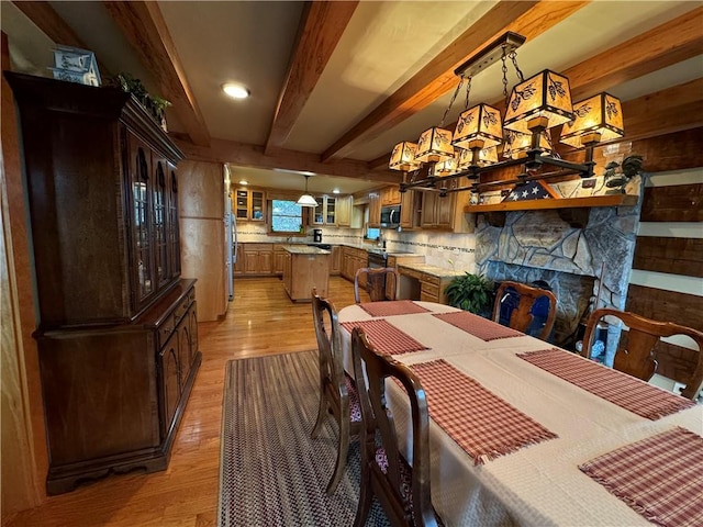 dining room featuring a stone fireplace, light hardwood / wood-style floors, and beamed ceiling