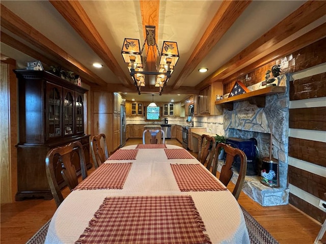 dining space with beam ceiling, light hardwood / wood-style floors, and a stone fireplace