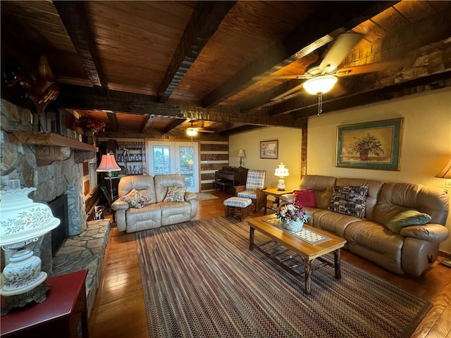 living room with wood-type flooring, beam ceiling, ceiling fan, and a stone fireplace