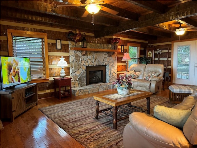 living room featuring ceiling fan, a stone fireplace, hardwood / wood-style flooring, and wooden walls