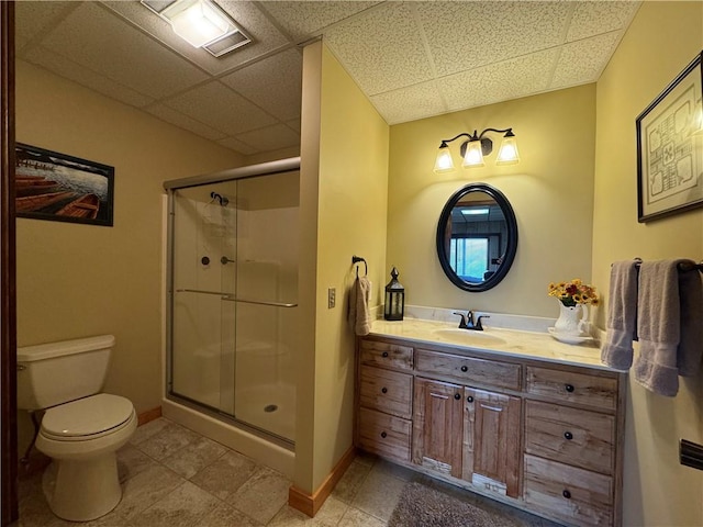 bathroom featuring vanity, a drop ceiling, a shower with door, toilet, and tile patterned floors