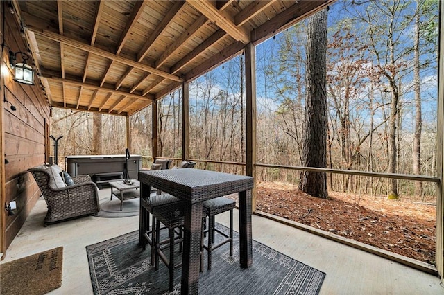 view of patio / terrace featuring a hot tub, outdoor dining area, and a view of trees