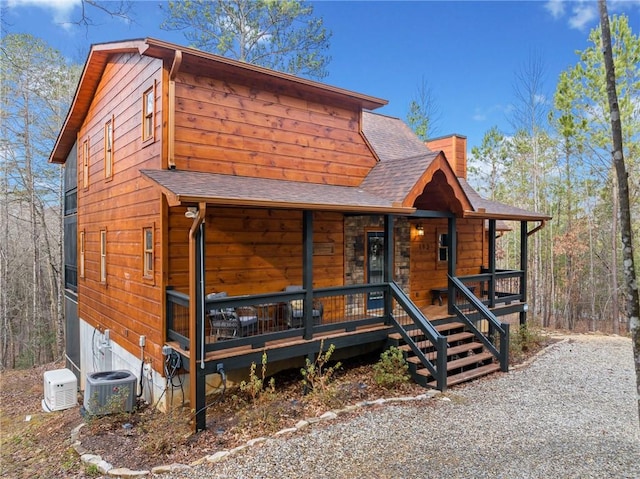 chalet / cabin featuring covered porch, a chimney, central AC unit, and roof with shingles