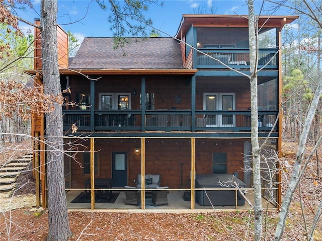 back of property with a balcony, a shingled roof, a sunroom, a chimney, and a patio area