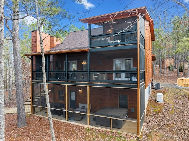 rear view of house with a balcony, a sunroom, a chimney, roof with shingles, and central air condition unit