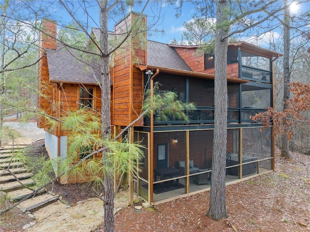 rear view of house with a sunroom, roof with shingles, and a chimney