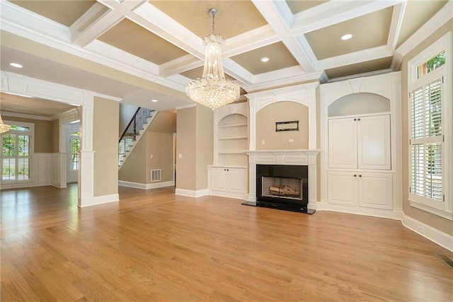 unfurnished living room with built in features, a fireplace with raised hearth, a notable chandelier, and stairway