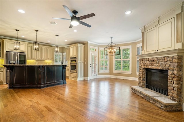 kitchen featuring stainless steel appliances, cream cabinetry, a fireplace, and light stone counters