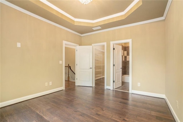 unfurnished bedroom with wood finished floors, baseboards, ornamental molding, a tray ceiling, and ensuite bath