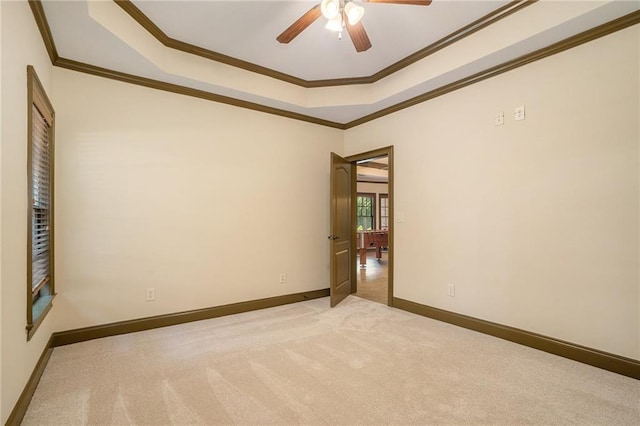 spare room featuring crown molding, a raised ceiling, light colored carpet, a ceiling fan, and baseboards