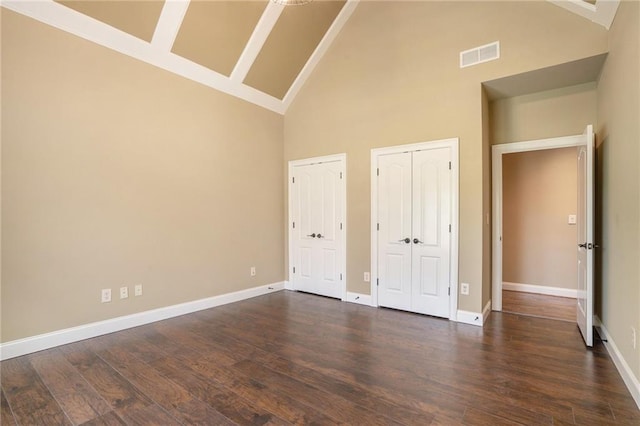 unfurnished bedroom featuring dark wood-style floors, baseboards, visible vents, and multiple closets