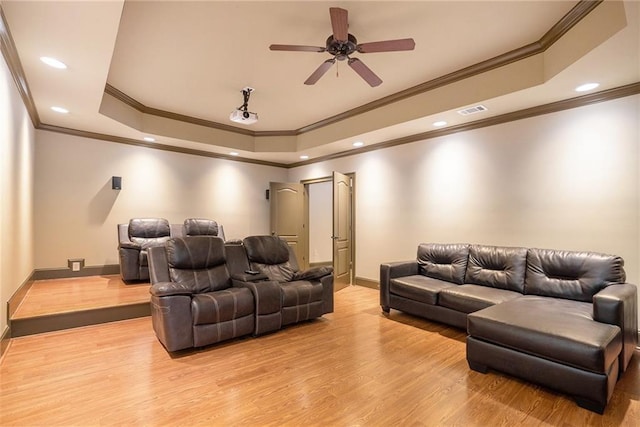 cinema room featuring light wood-style floors, a tray ceiling, visible vents, and baseboards