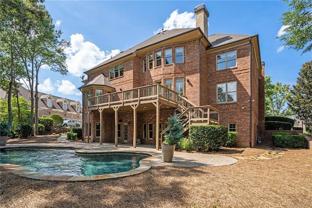 rear view of property with brick siding, a patio, a chimney, and a wooden deck