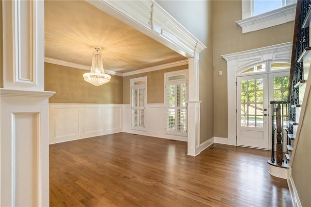 foyer entrance with a chandelier, dark wood-style flooring, a wainscoted wall, and crown molding