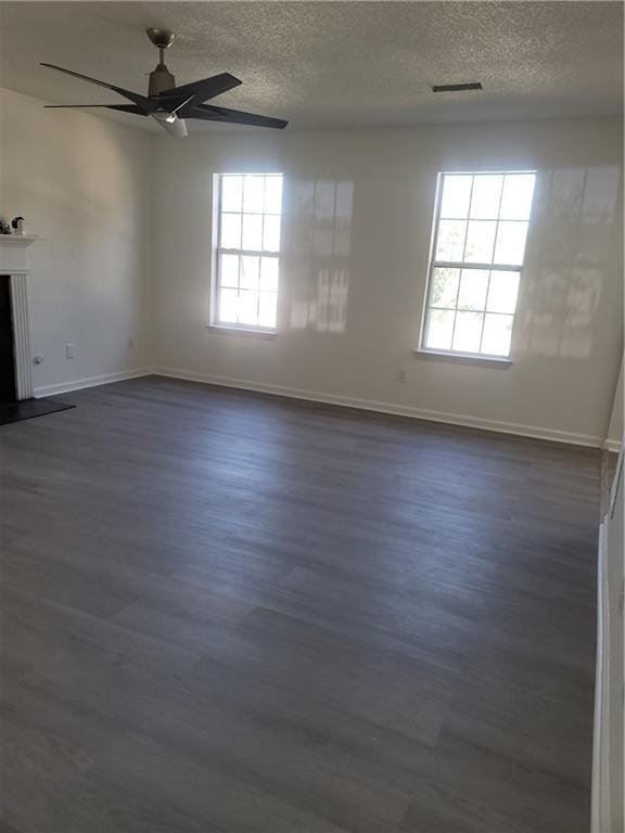 empty room featuring a textured ceiling, plenty of natural light, ceiling fan, and dark wood-type flooring