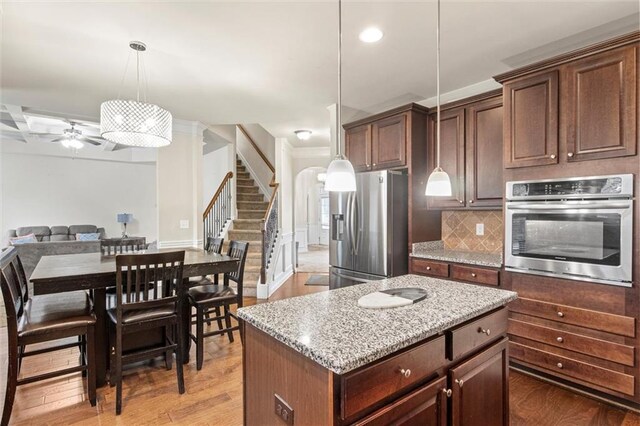 kitchen featuring ceiling fan, a kitchen island, appliances with stainless steel finishes, decorative light fixtures, and light hardwood / wood-style floors