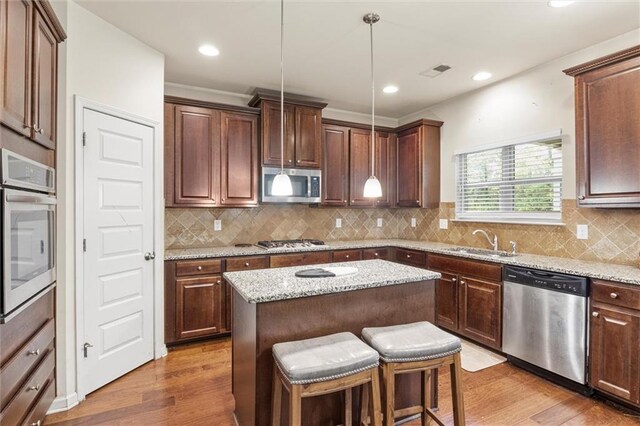 kitchen featuring decorative light fixtures, a center island, wood-type flooring, and stainless steel appliances