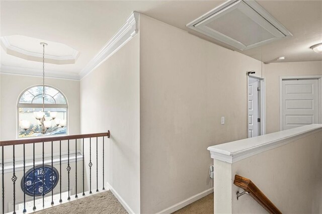 hall featuring carpet flooring, a raised ceiling, ornamental molding, and an inviting chandelier