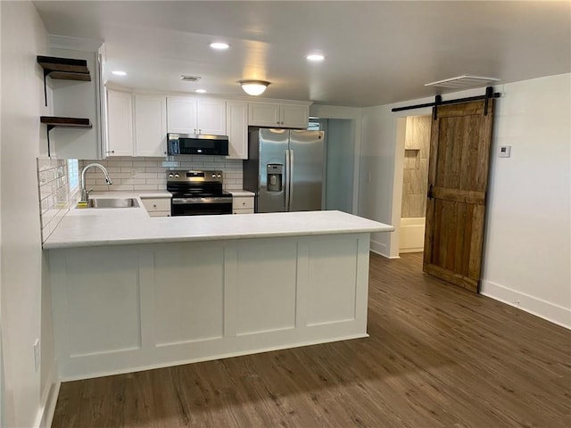 kitchen with sink, a barn door, appliances with stainless steel finishes, white cabinetry, and kitchen peninsula