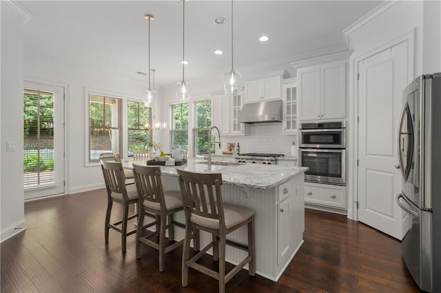 kitchen with decorative backsplash, a sink, under cabinet range hood, stainless steel appliances, and white cabinetry