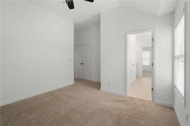 unfurnished bedroom with baseboards, multiple windows, vaulted ceiling, and light carpet