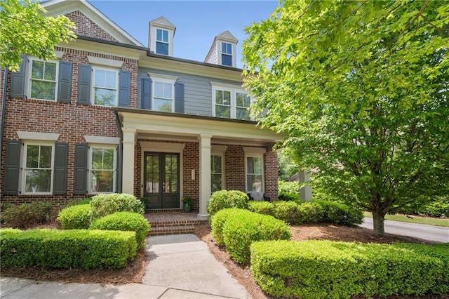 view of front facade with covered porch, brick siding, and french doors