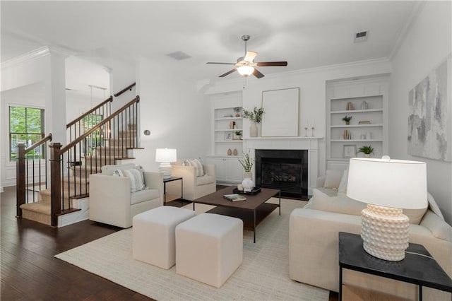 living room featuring crown molding, ceiling fan, built in features, wood finished floors, and visible vents