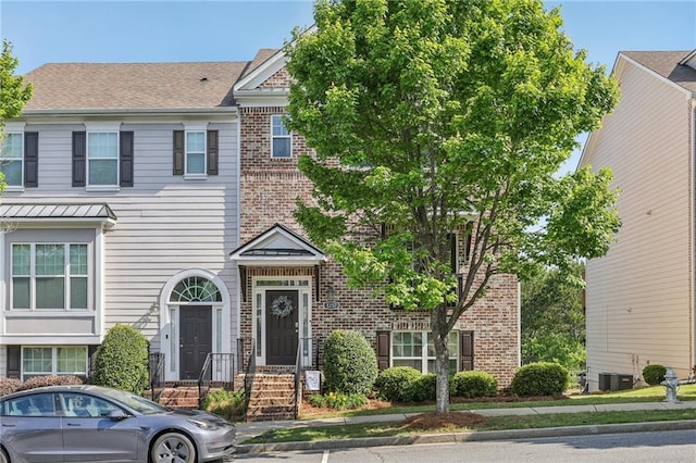townhome / multi-family property with central air condition unit, a shingled roof, and brick siding