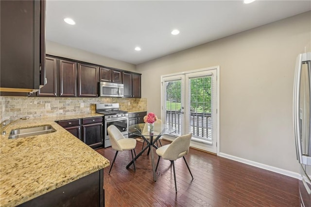 kitchen featuring light stone countertops, a sink, dark brown cabinetry, backsplash, and stainless steel appliances