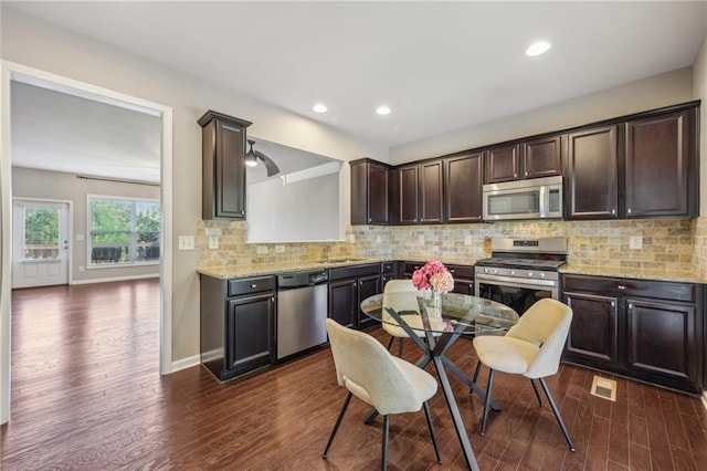 kitchen featuring a sink, dark brown cabinetry, decorative backsplash, dark wood-style floors, and appliances with stainless steel finishes