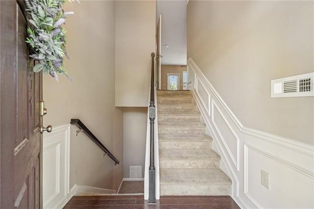 stairs with visible vents, a decorative wall, and wainscoting