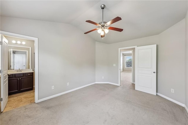 unfurnished bedroom featuring lofted ceiling, baseboards, ensuite bathroom, a sink, and light colored carpet