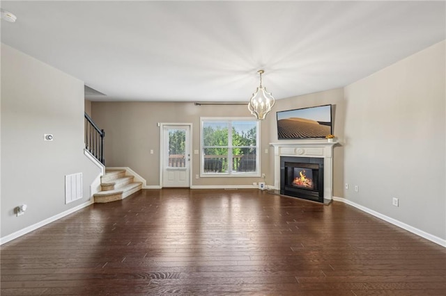 unfurnished living room featuring wood-type flooring, visible vents, baseboards, a glass covered fireplace, and a chandelier