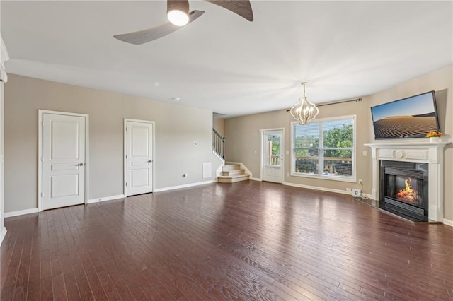unfurnished living room featuring baseboards, a glass covered fireplace, ceiling fan with notable chandelier, stairs, and hardwood / wood-style floors