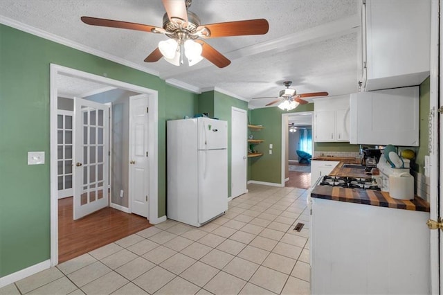 kitchen with a textured ceiling, crown molding, light tile patterned floors, white refrigerator, and white cabinetry