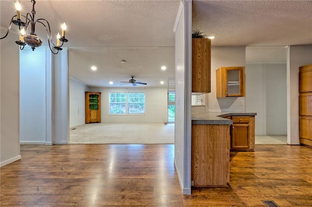 kitchen with brown cabinets, a textured ceiling, wood finished floors, dark countertops, and a chandelier