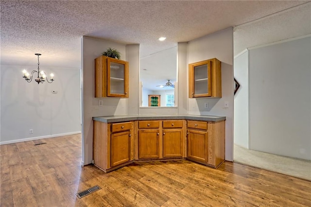 kitchen with brown cabinetry, light wood-style floors, glass insert cabinets, a textured ceiling, and a chandelier